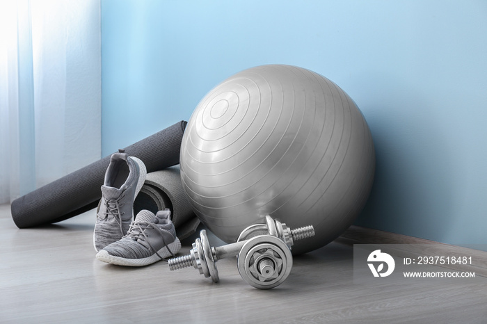 Set of sports equipment with fitness ball and shoes near color wall