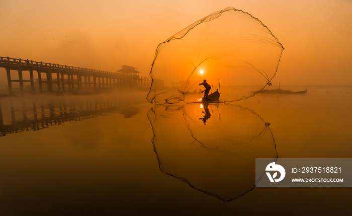 Silhouette Asian fisherman on wooden boat casting a net for freshwater fish at U Bein Bridge,Mandala