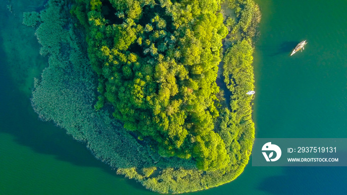 Birds eye view of the green island in the middle of the lake in a daylight.