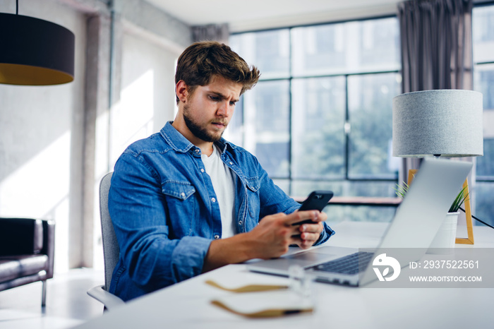 Young man with smartphone in his hands. Modern businessman at sunny office. Freelancer at work.