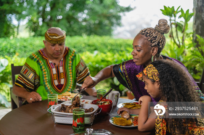 Horizontal de una hermosa familia afrocaribeña sentados a la mesa en exterior compartiendo un delici