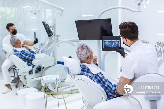 Portrait of handsome smiling dentist looking at x-ray image of his patient.