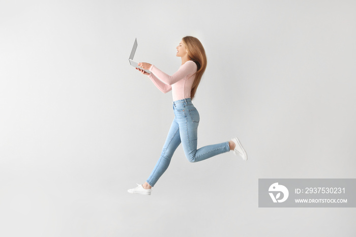 Jumping young woman with laptop on light background