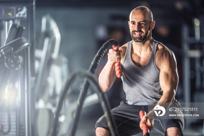 Muscular man exercising with battle ropes at the fitness gym