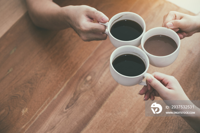 Top view image of three people clinking coffee cups on wooden table in cafe