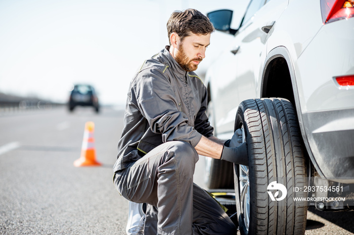 Handsome road assistance worker in uniform changing car wheel on the highway