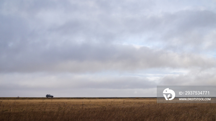 Сar goes on the horizon in the background of the cloudy sky