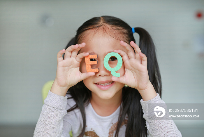 Adorable little Asian child girl holding alphabet EQ (Emotional Quotient) text on her face. Educatio