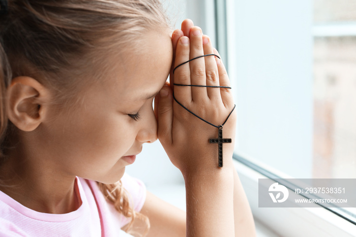 Praying little girl near window