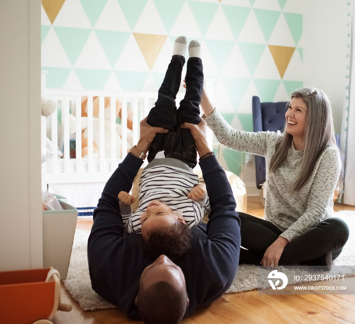 Happy mother sitting by father picking up son upside down while lying on rug at home