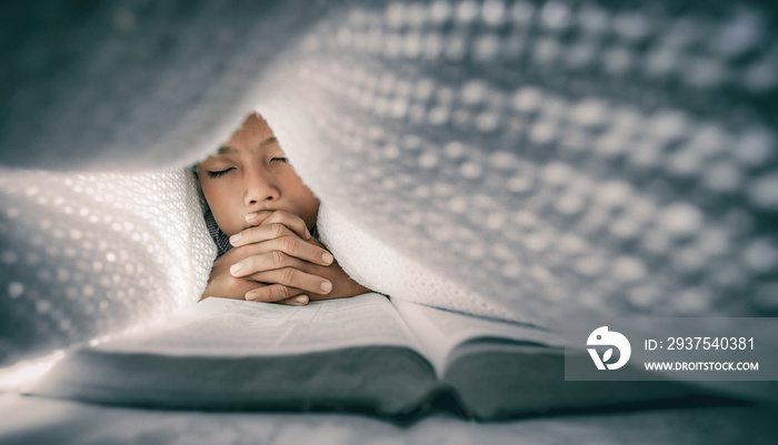 Focus at face. Christian boy reading bible and praying under the covers at night.