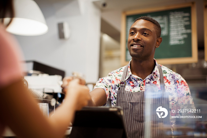 Cropped hand of female customer making card payment to barista at counter in cafe