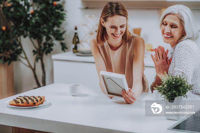 Happy daughter with mother are admiring photo in kitchen