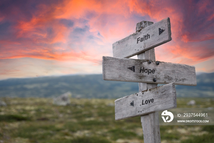 faith hope love text engraved in wooden signpost outdoors in nature during sunset and pink skies.