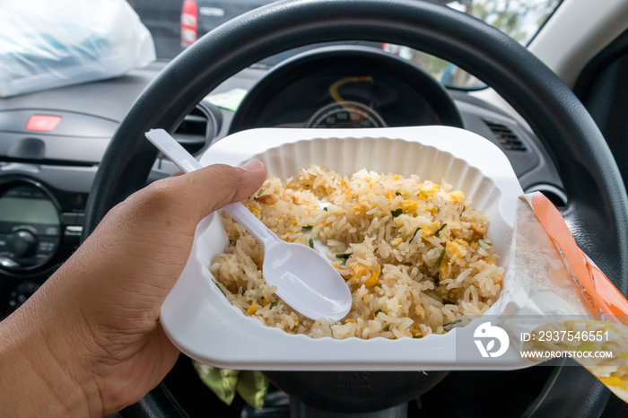 Close up of drivers hand at the wheel while eating fast food in the traffic