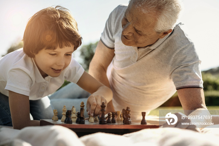 Making a move. Joyful concentrated young boy playing chess with his grandpa and making a move while 