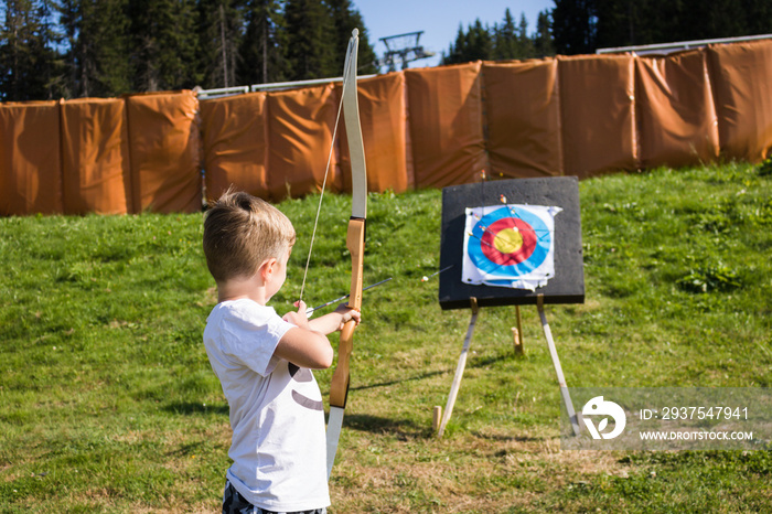 Little boy using bow and arrow and aiming at the target.