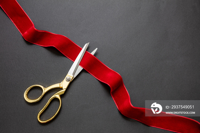 Grand opening, ribbon cut, overhead of gold scissors cutting red velvet ribbon on black