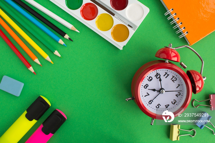 School stationery and red alarm clock on the green background.Top view. Copy space.