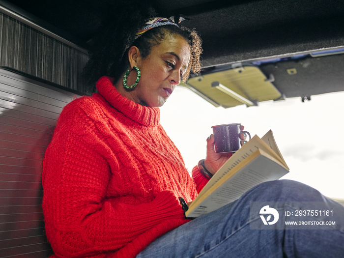 Woman sitting in back of van and reading book