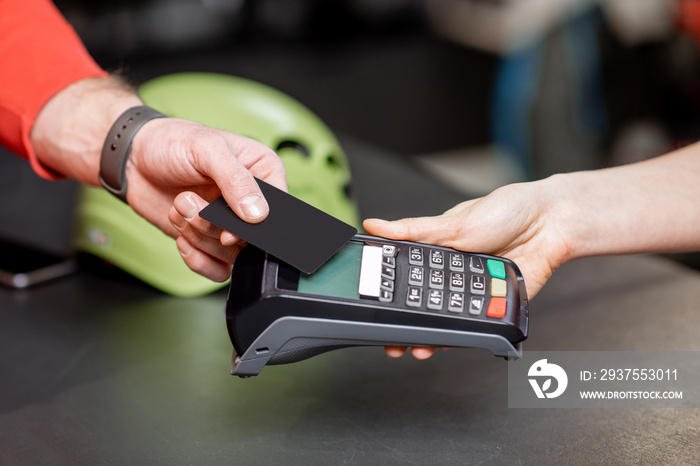 Man making purchase with bank card and cash register at the counter of the sports shop, close-up vie