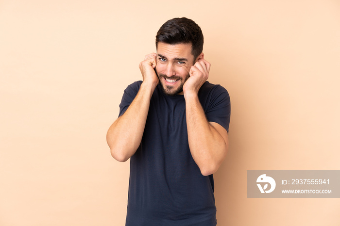 Caucasian handsome man isolated on beige background frustrated and covering ears