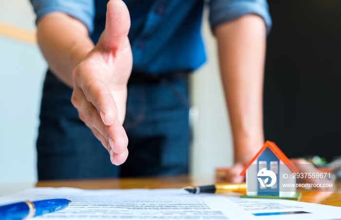 房屋销售员伸出手握手，笔和房屋平面图上的房屋模型。