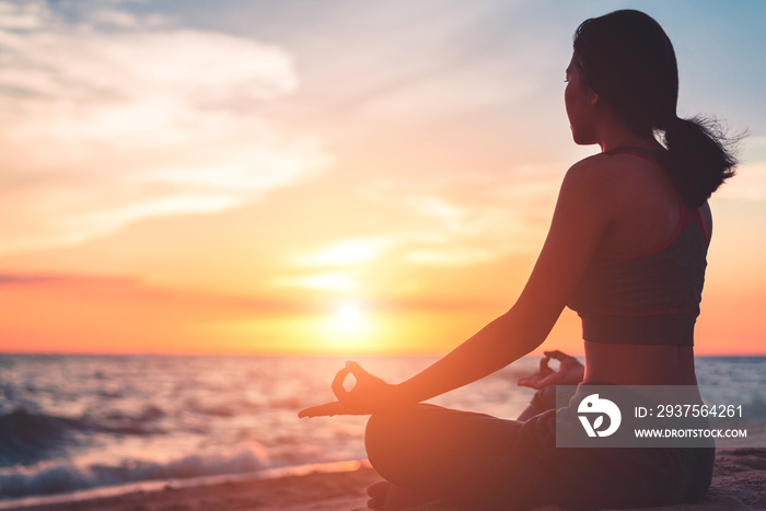 Silhouette young woman practicing yoga on the beach at sunset.