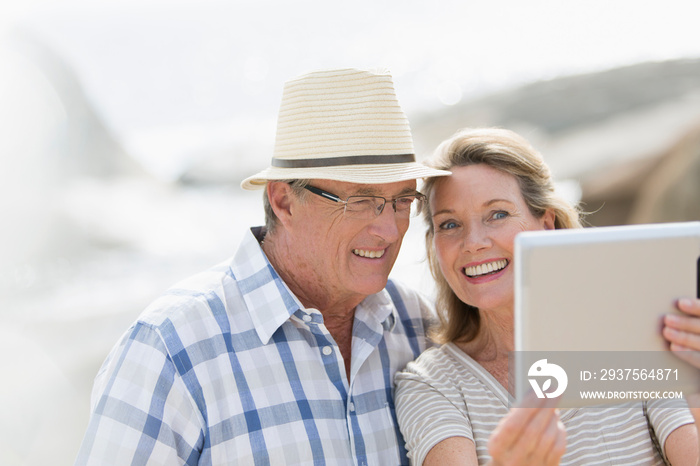 Happy senior couple taking selfie with digital tablet on sunny beach