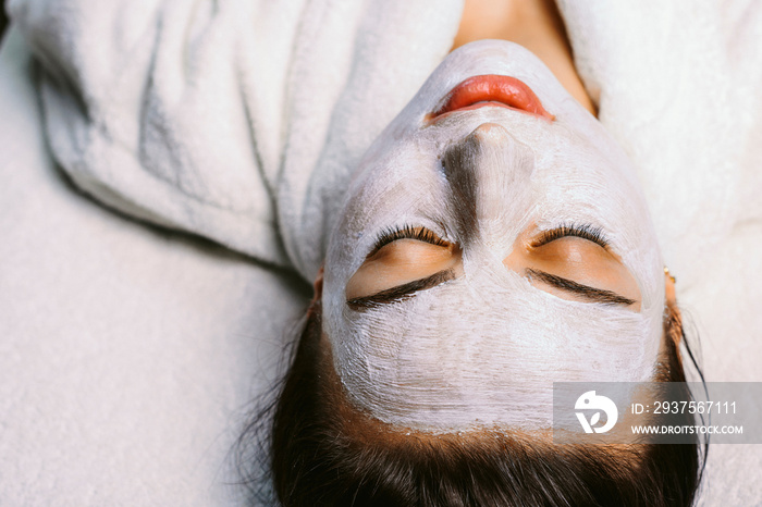 Beautiful caucasian girl resting with closed eyes in a spa center while on her face is applied a whi