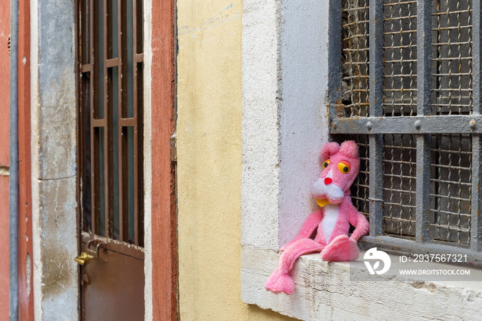 意大利老城区老房子窗户前丢弃的粉红色老虎玩偶