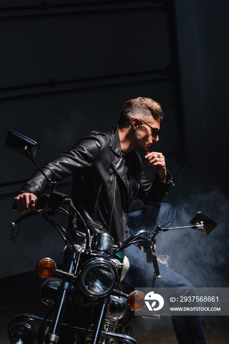 classic biker in sunglasses sitting on motorbike in garage