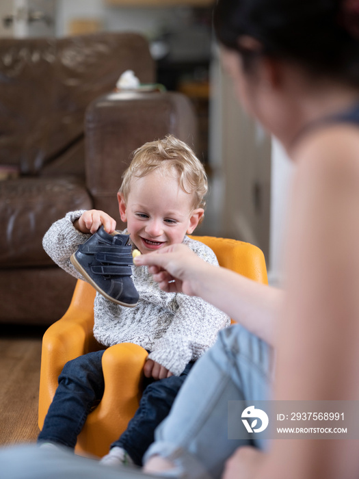 Smiling boy holding shoe and looking at it�