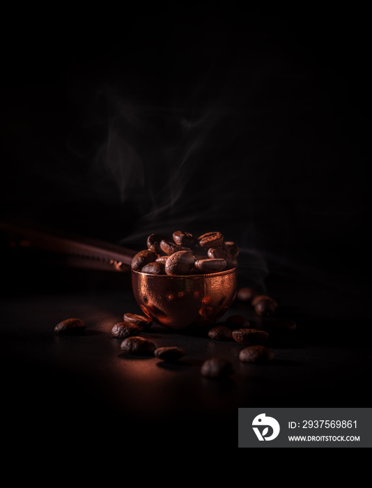 Roasted coffee beans in the copper spoon with smoke on dark background. Concept to recognize the aro