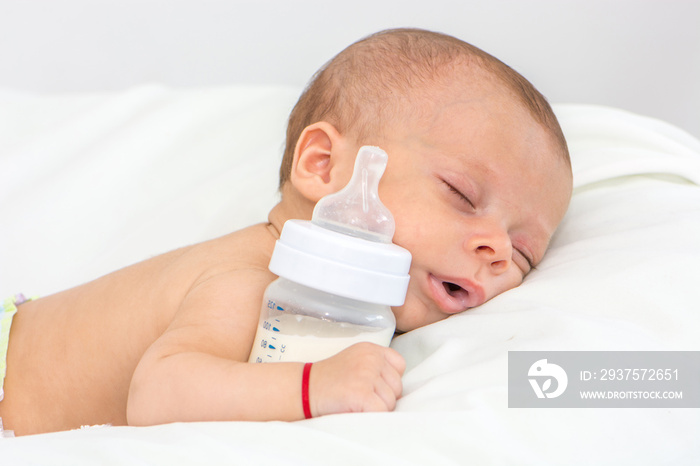 newborn baby curled up sleeping on a blanket with feeding bottle