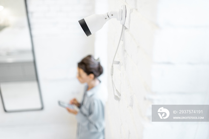 Woman controls home video surveillance with a smartphone indoors, view from the above and ip camera 