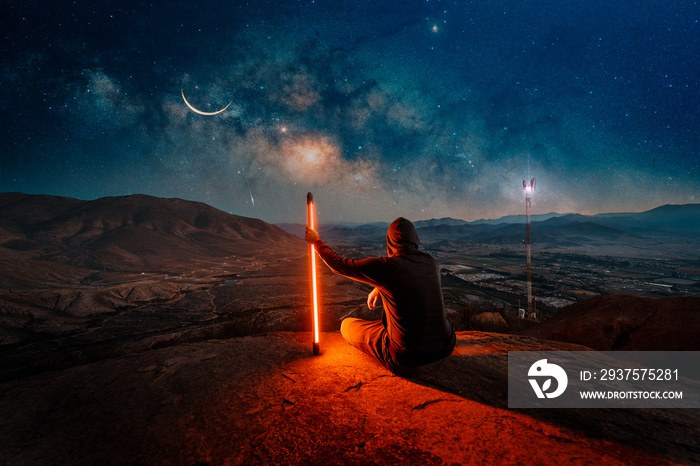 man sitting on the top of the mountain with led light under the milky way watching the sky