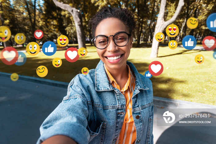 快乐的千禧一代非裔美国女士，穿着休闲装，戴着眼镜，在公园里为社交网络自拍