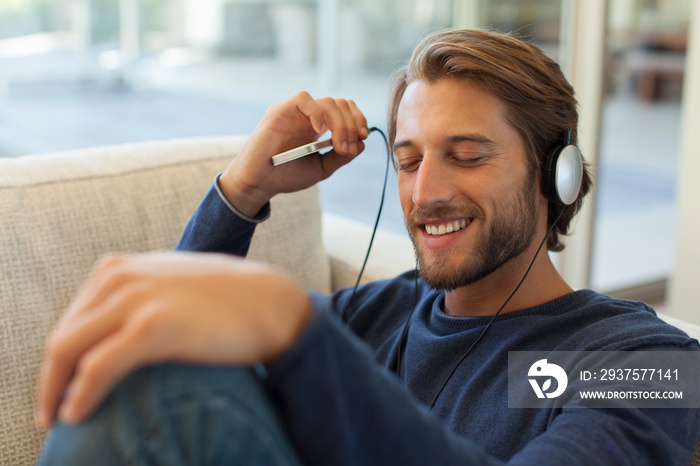 微笑的年轻人戴着耳机和智能手机听音乐
