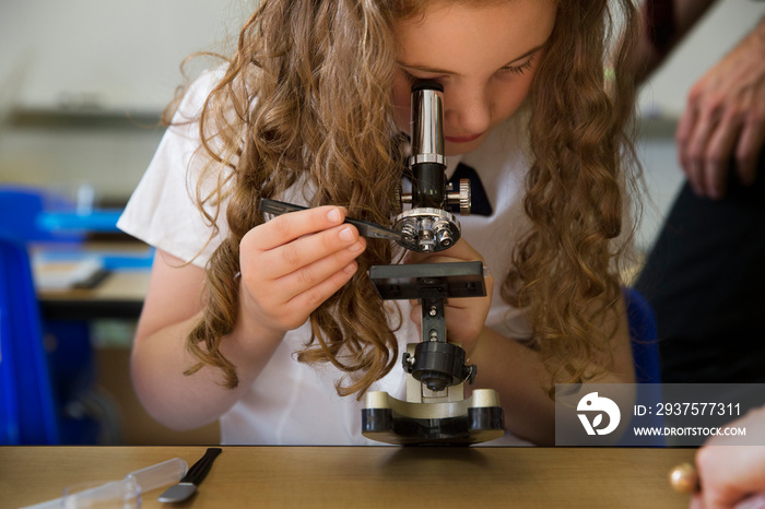 Blond school girl using microscope in classroom