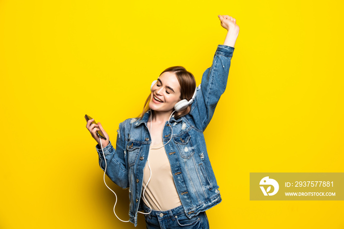 Happy cheerful woman wearing headphones listening to music from smartphone studio shot isolated on y