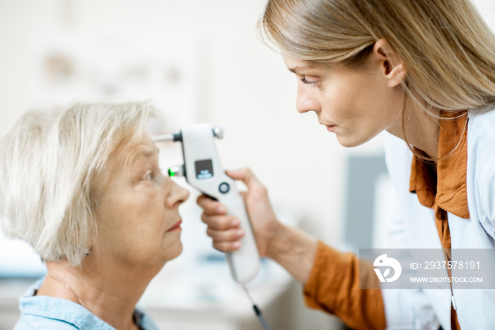 Female ophthalmologist measuring the eye pressure with modern tonometer to a senior patient in the m