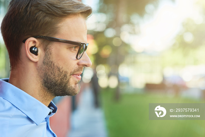 Side view of a young handsome businessman listening to music with wireless earphones