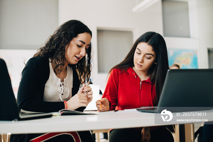 Female friends studying together while sitting in classroom at university