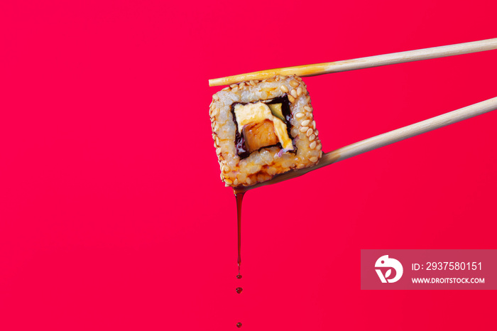 succulent roll between chopsticks on a colored background, drops of soy sauce dripping from sushi, f