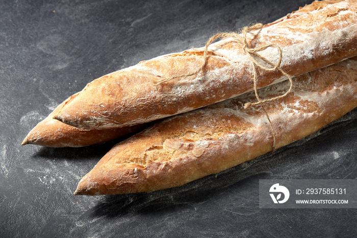 food, baking and cooking concept - pile of baguette bread loaves tied with rope on table over dark b