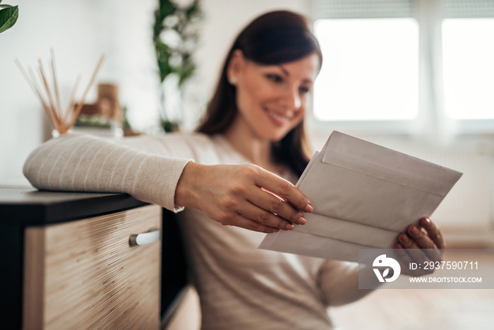 Beautiful woman reading a letter at home, close-up. Focus on the foreground, on the hands holding le