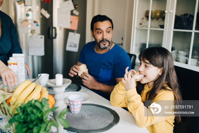 Father and daughter eating breakfast while sitting at table in kitchen