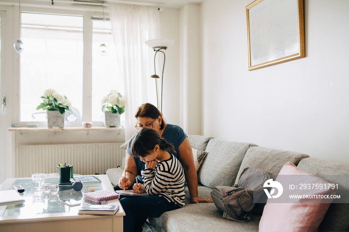 Senior woman assisting girl in homework on sofa at living room