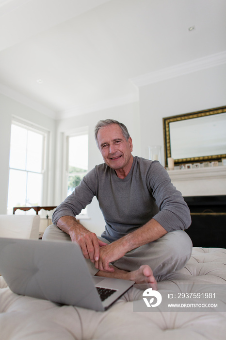 Portrait senior man using laptop on ottoman